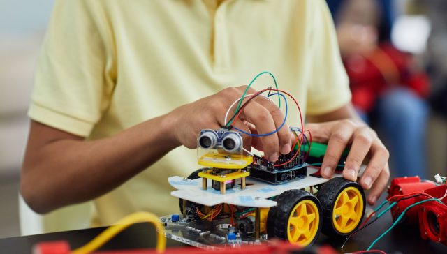 A child engaging in a STEM activity by assembling a robotic toy car featuring electronics and wiring.
