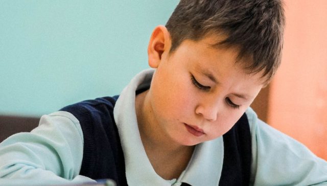 Bir çocuğun derslik ortamında titizlikle çalışması, konsantrasyon ve öğrenmeyi sergiliyor.