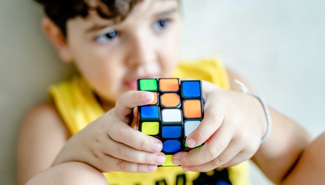 Young boy holding and concentrating on solving a colorful Rubik's Cube indoors.