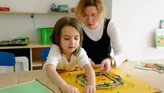A child and teacher work together on an educational activity in a classroom setting.