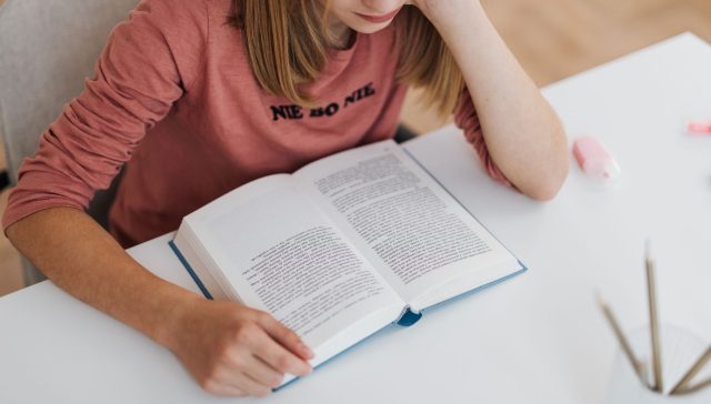A woman reading a book at a white desk, focused and engaged in a casual setting.