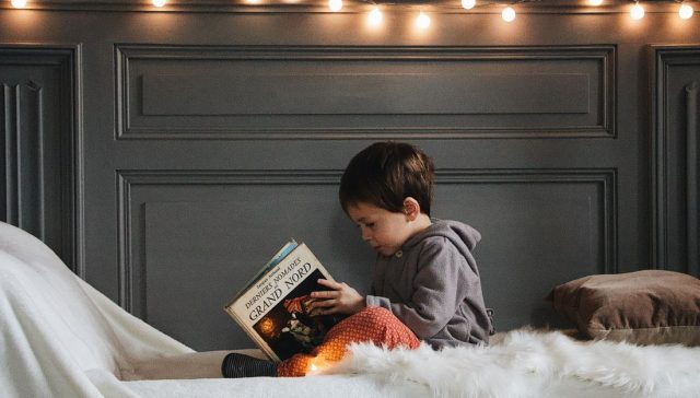Sıcak ip ışıkları ve yumuşak dokularla dolu rahat bir yatak odasında genç bir çocuk kitap okuyor.