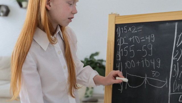 Genç kız, rahat bir sınıf ortamında kara tahtada matematik problemlerine odaklanıyor.