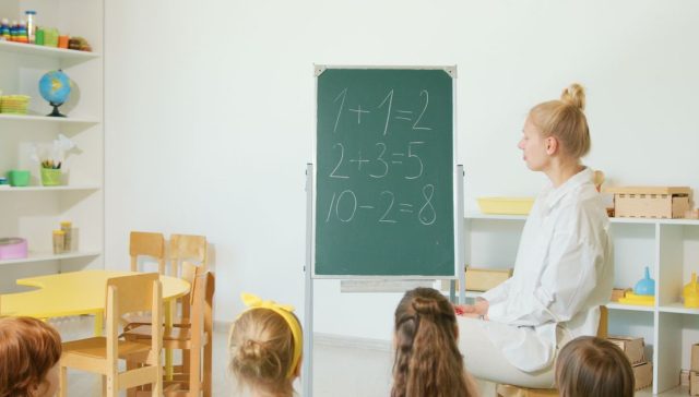 Renkli bir sınıfta oturan çocuklar, bir öğretmenden temel matematik öğreniyor.
