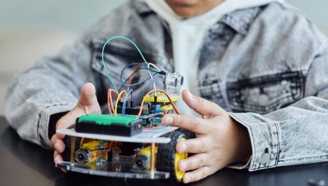 Bir çocuğun teller ve tekerleklerle DIY robotik projesi üzerinde çalışması, yenilik ve yaratıcılığı sergiliyor.